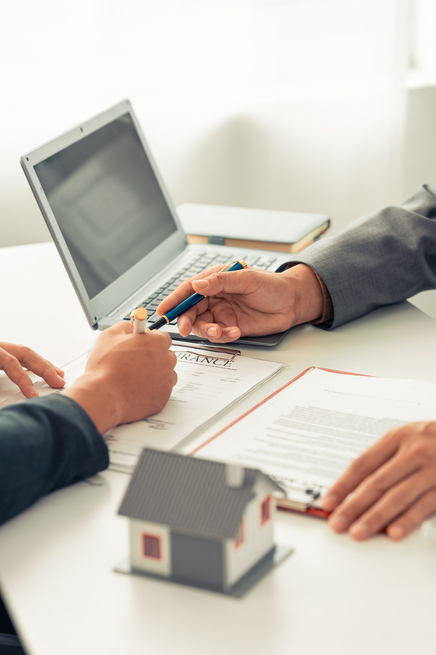 Hands discussing real estate contract with laptop.